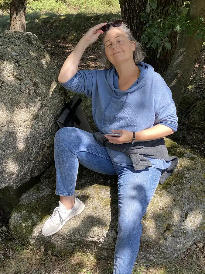 Constanze sitzt auf einem Fels unter einem Baum