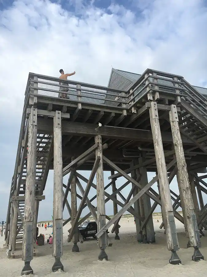 Pfahlbau am Strand von St. Peter Ording, ein Mann steht oben und macht ein Selfie